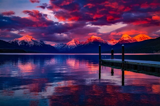 an outdoors shot of water with snow capped mountains in the back, a purple hue